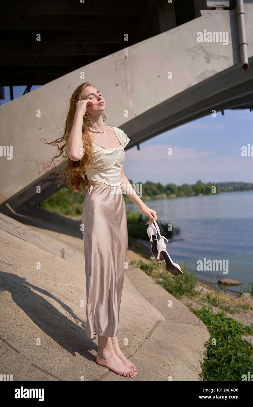 a beautiful teenage girl in a silk skirt and corset in the old money style.  Fashion photoshoot under the bridge. Stock Photo