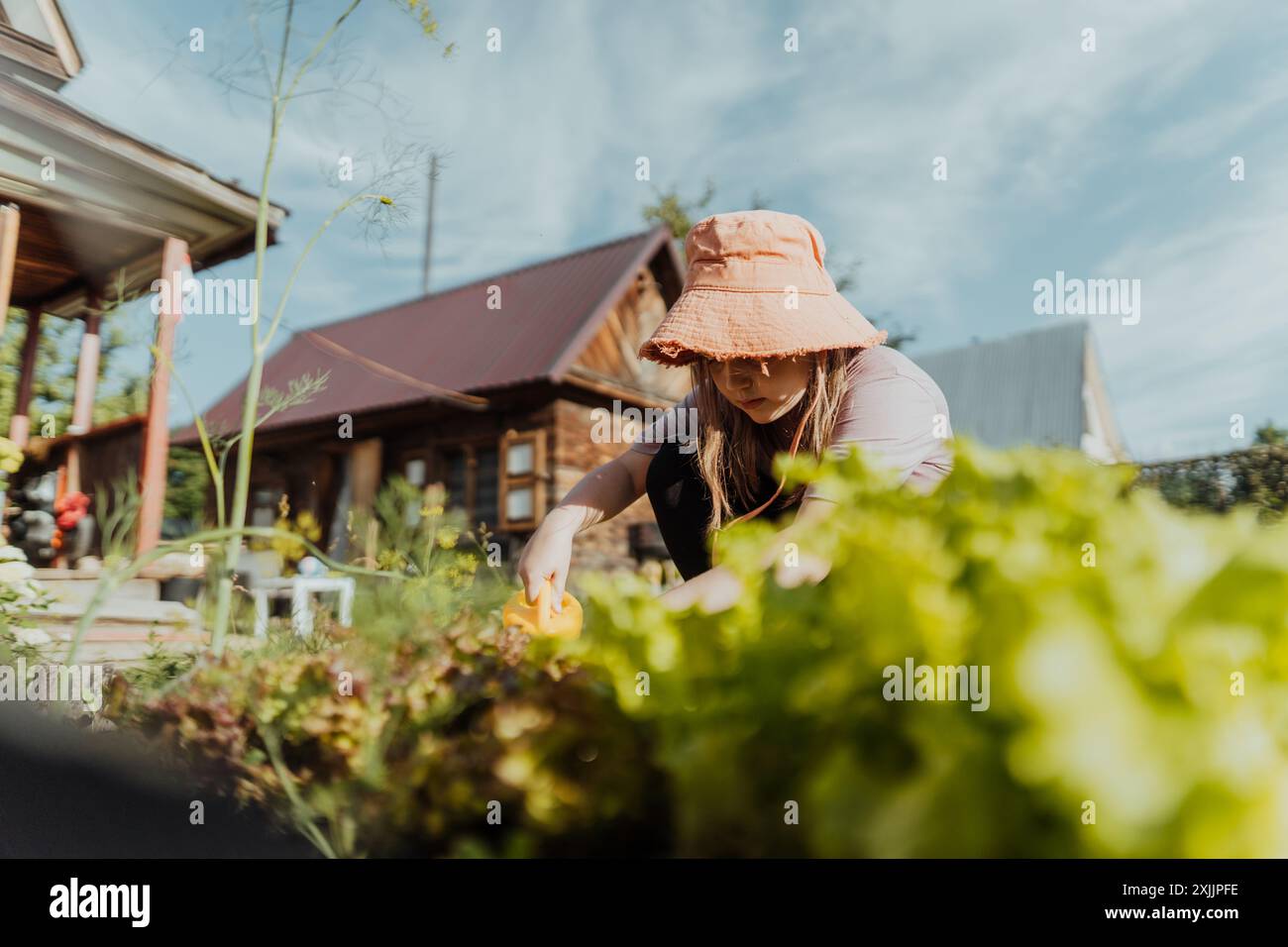 Smiling girl nurturing plants with a yellow watering can in the garden ...