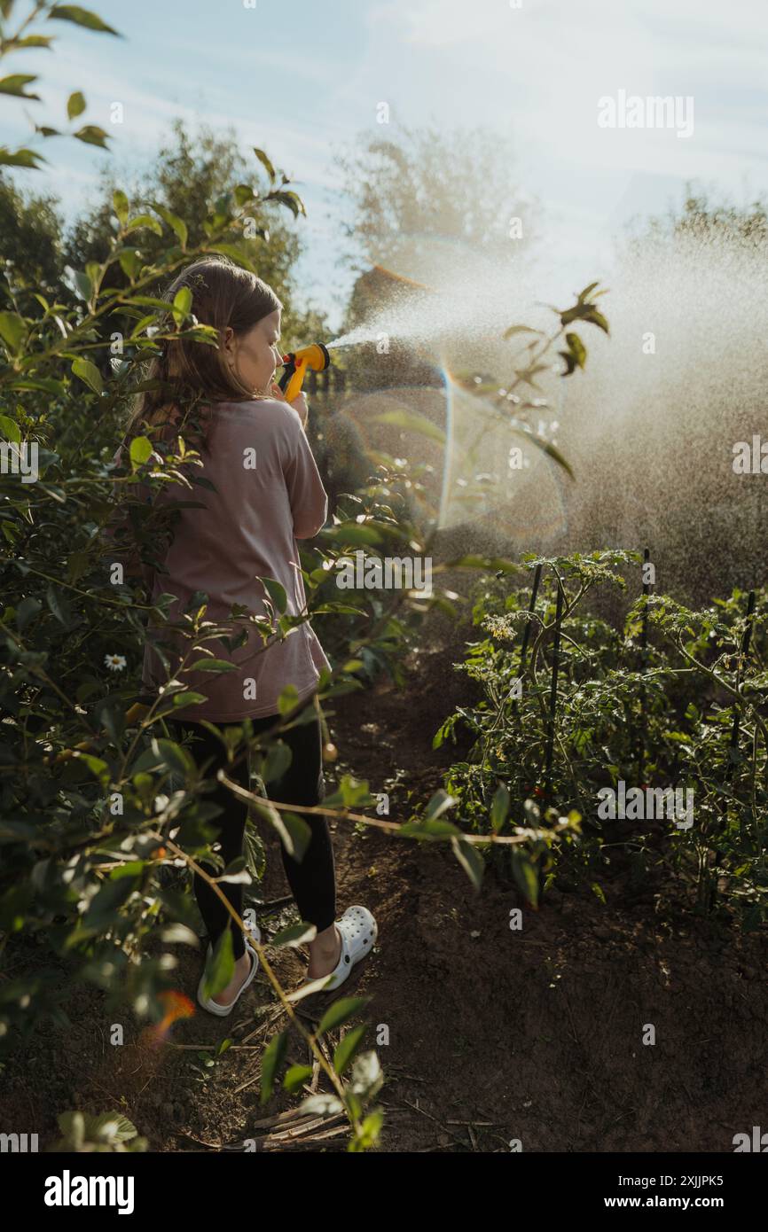 Young girl with long hair is watering greens in vegetable garden Stock Photo