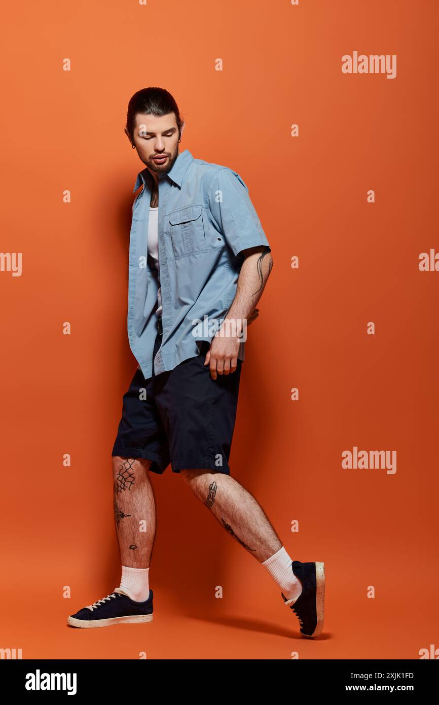 Stylish man in blue attire posing against vivid orange background Stock ...