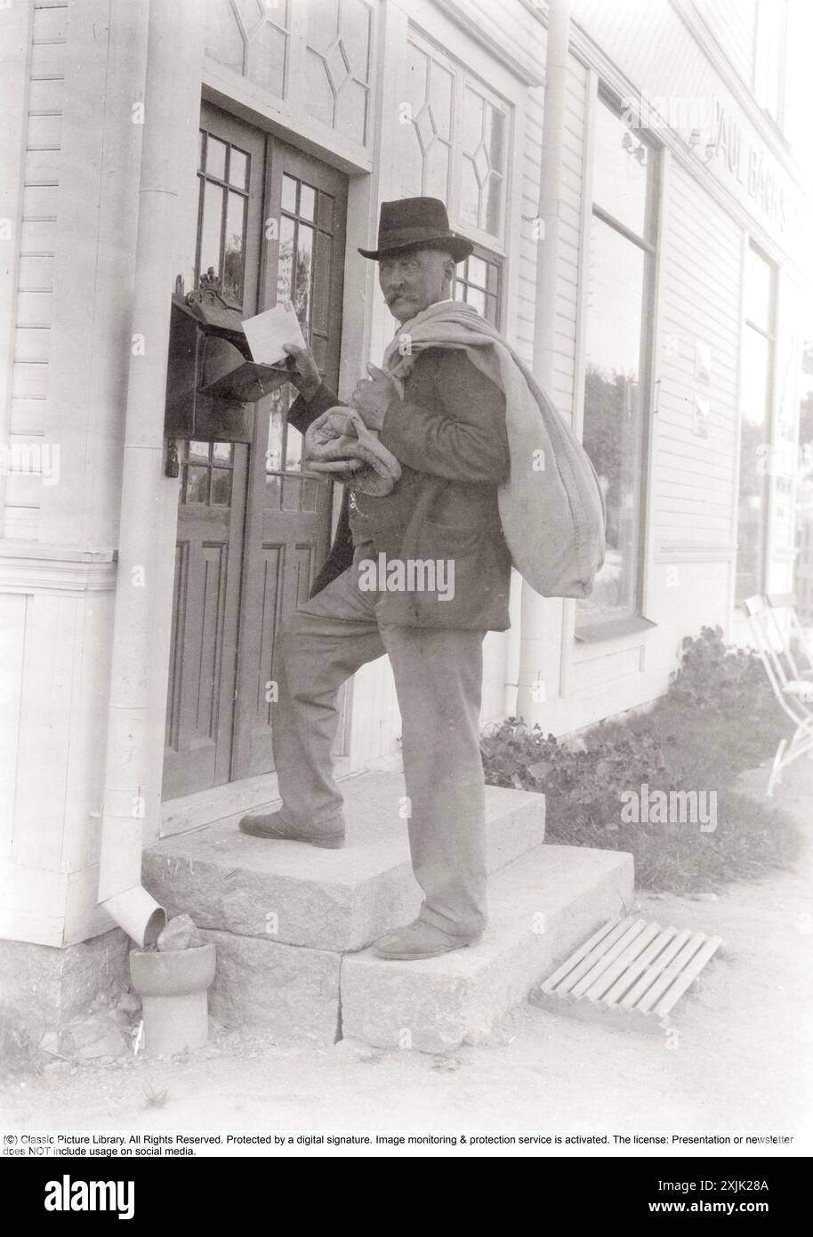 Postman delivering a letter at the turn of the century 1800-1900. He is carrying a sack containing the mail over his shoulder and back. Stock Photo