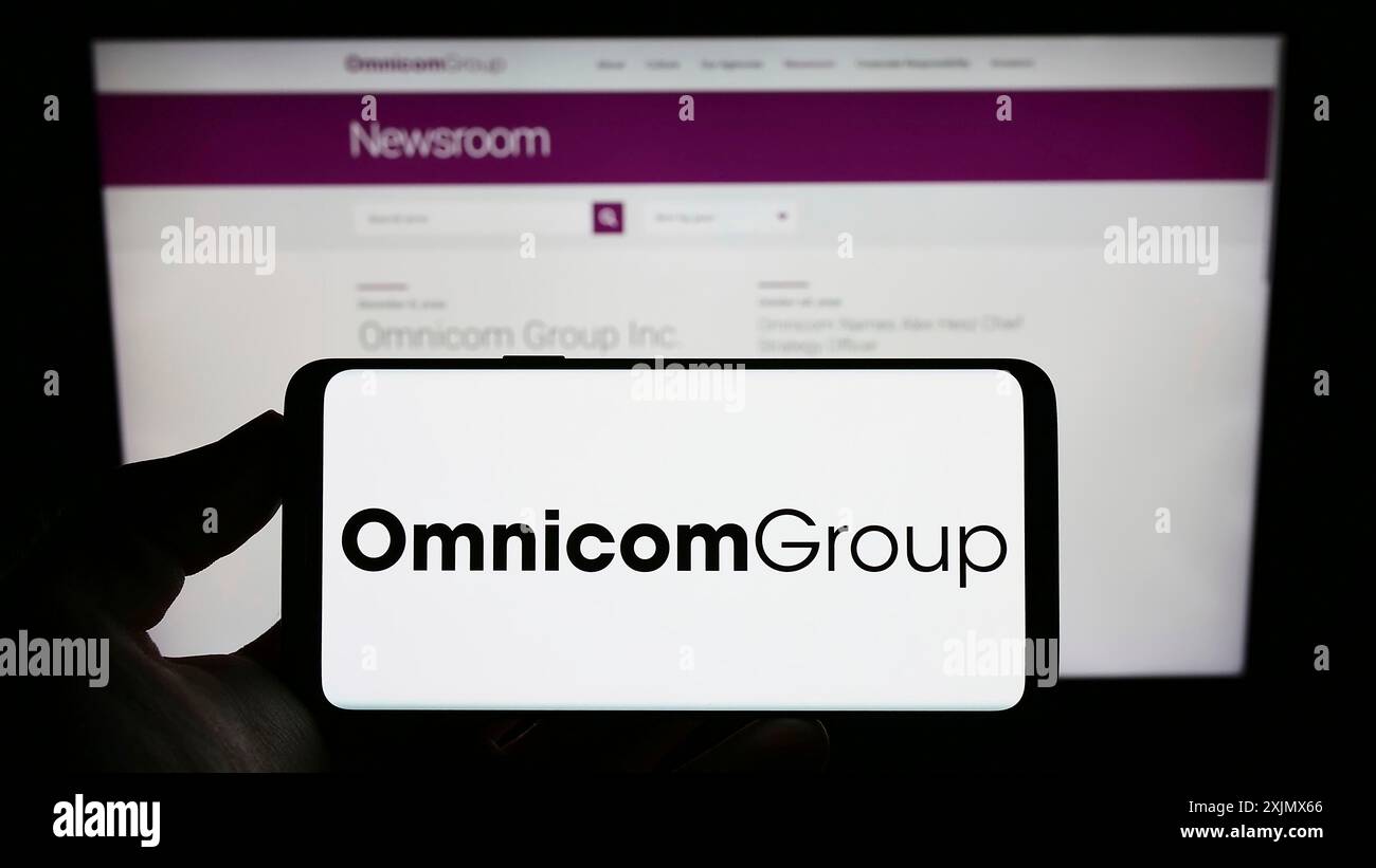 Stuttgart, Germany, 12-10-2022: Person holding cellphone with logo of US media company Omnicom Group Inc. on screen in front of business webpage. Stock Photo