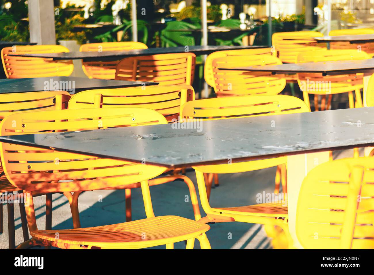 Row of yellow chairs are lined up in front of a table.  Chairs are empty and the table is wet after rain. The scene gives off a warm and inviting atmo Stock Photo