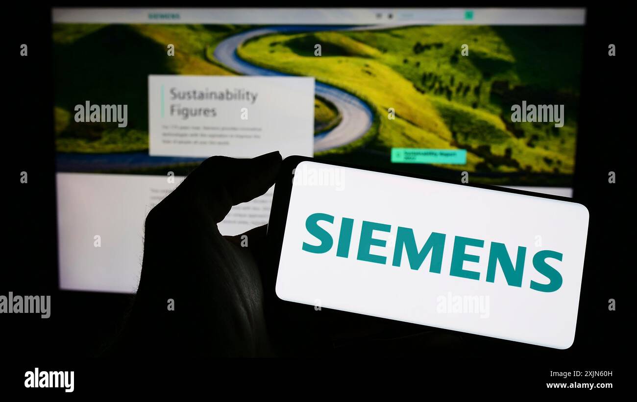 Stuttgart, Germany, 04-16-2023: Person holding cellphone with logo of German conglomerate Siemens AG on screen in front of business webpage. Focus on Stock Photo