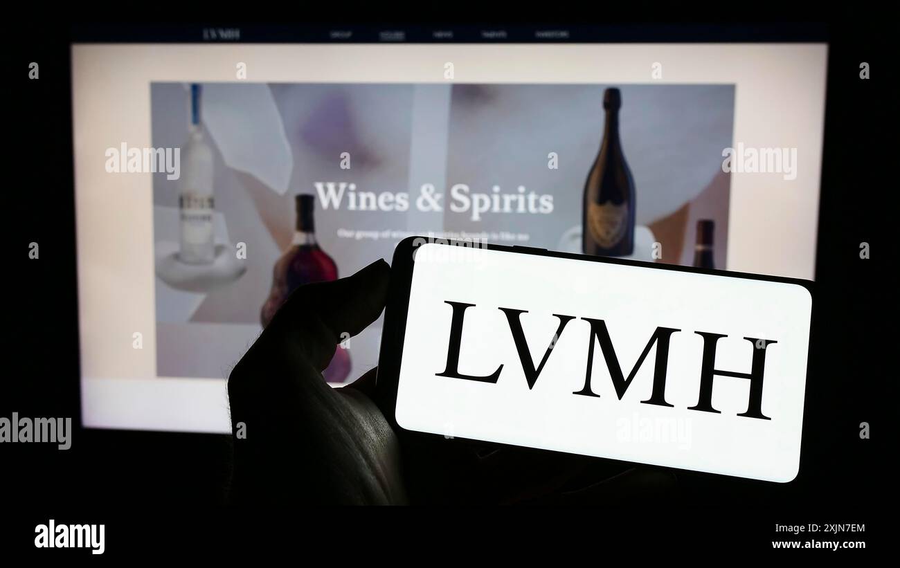 Stuttgart, Germany, 04-16-2023: Person holding cellphone with logo of company LVMH Moet Hennessy Louis Vuitton SE on screen in front of business Stock Photo