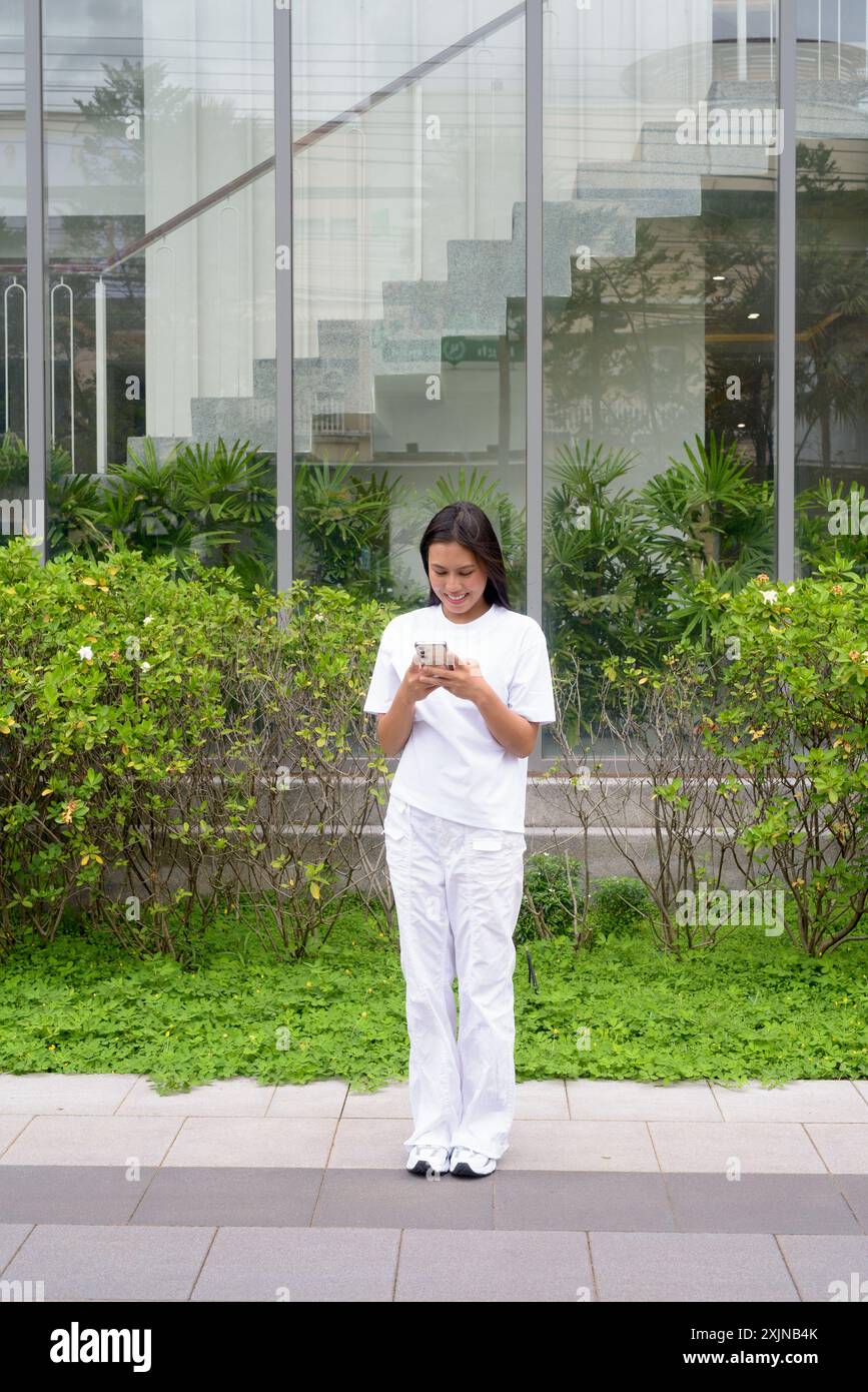 Young Thai Woman Smiling Outdoors Using Mobile Phone Concept Stock Photo