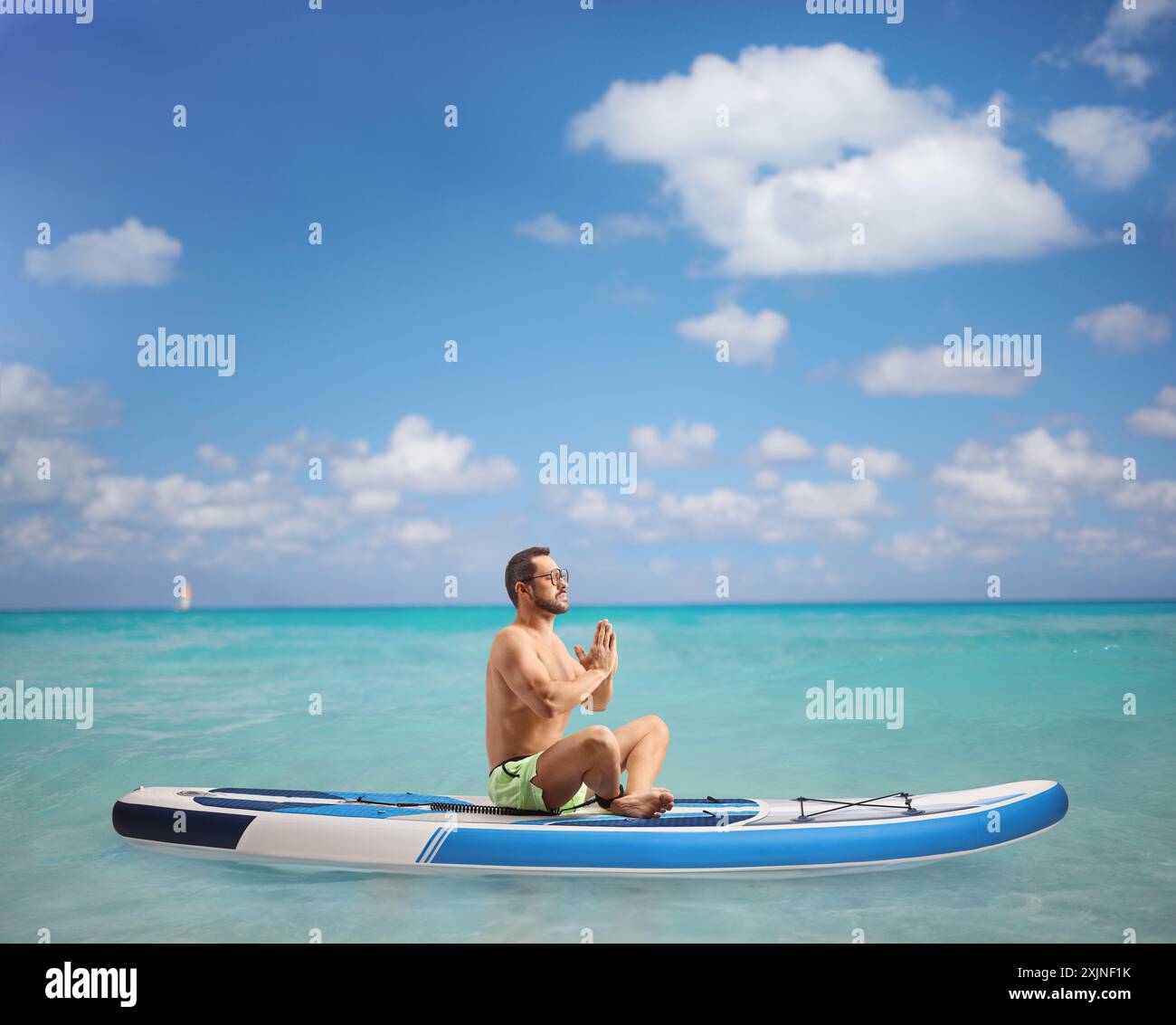 Full length profile shot of a man practicing meditation on a SUP in the sea Stock Photo