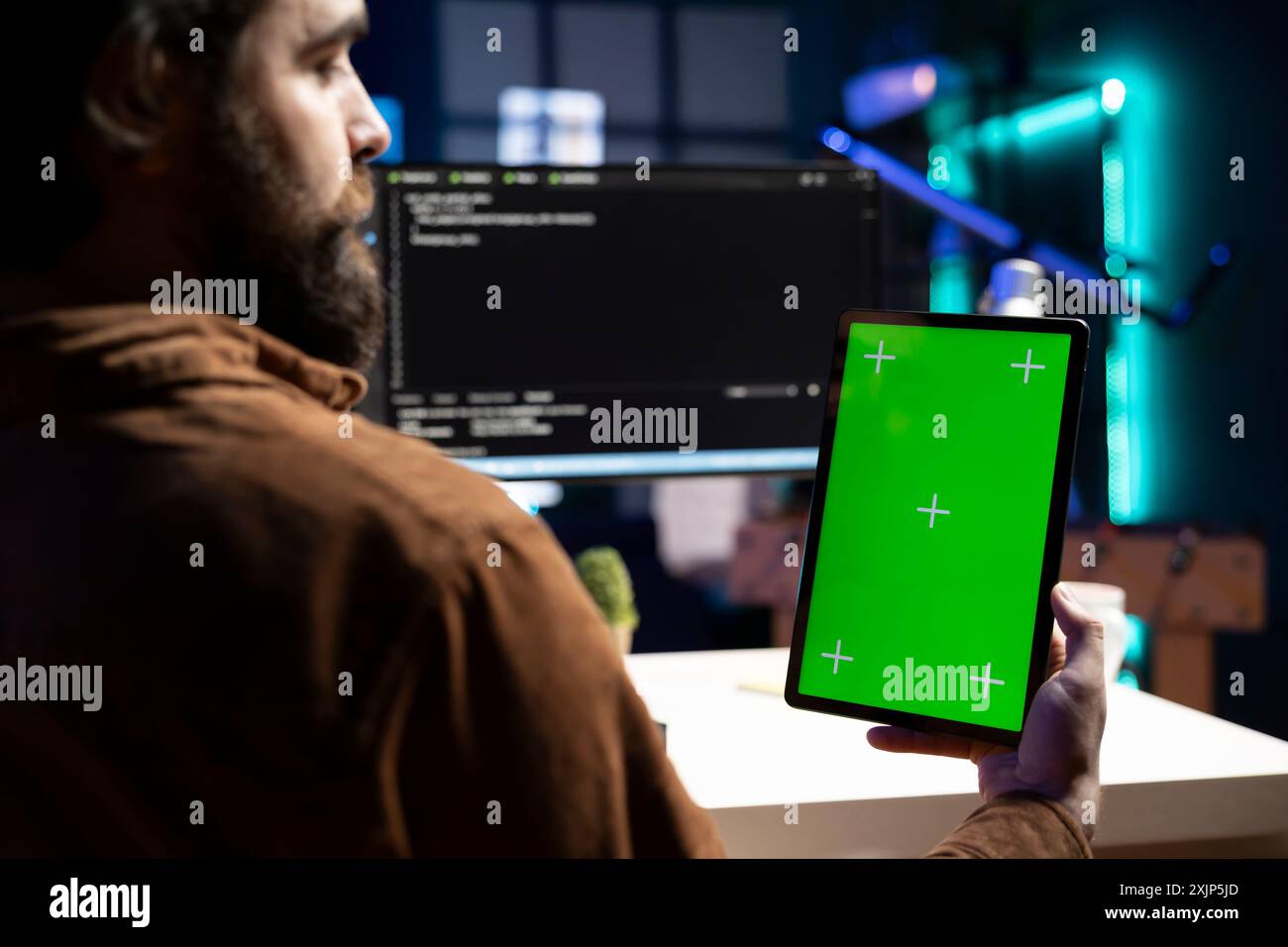 Admin doing software debugging using isolated screen tablet, checking errors in lines of code displayed on PC monitors. Man working from home fixing coding issues using chroma key portable device Stock Photo