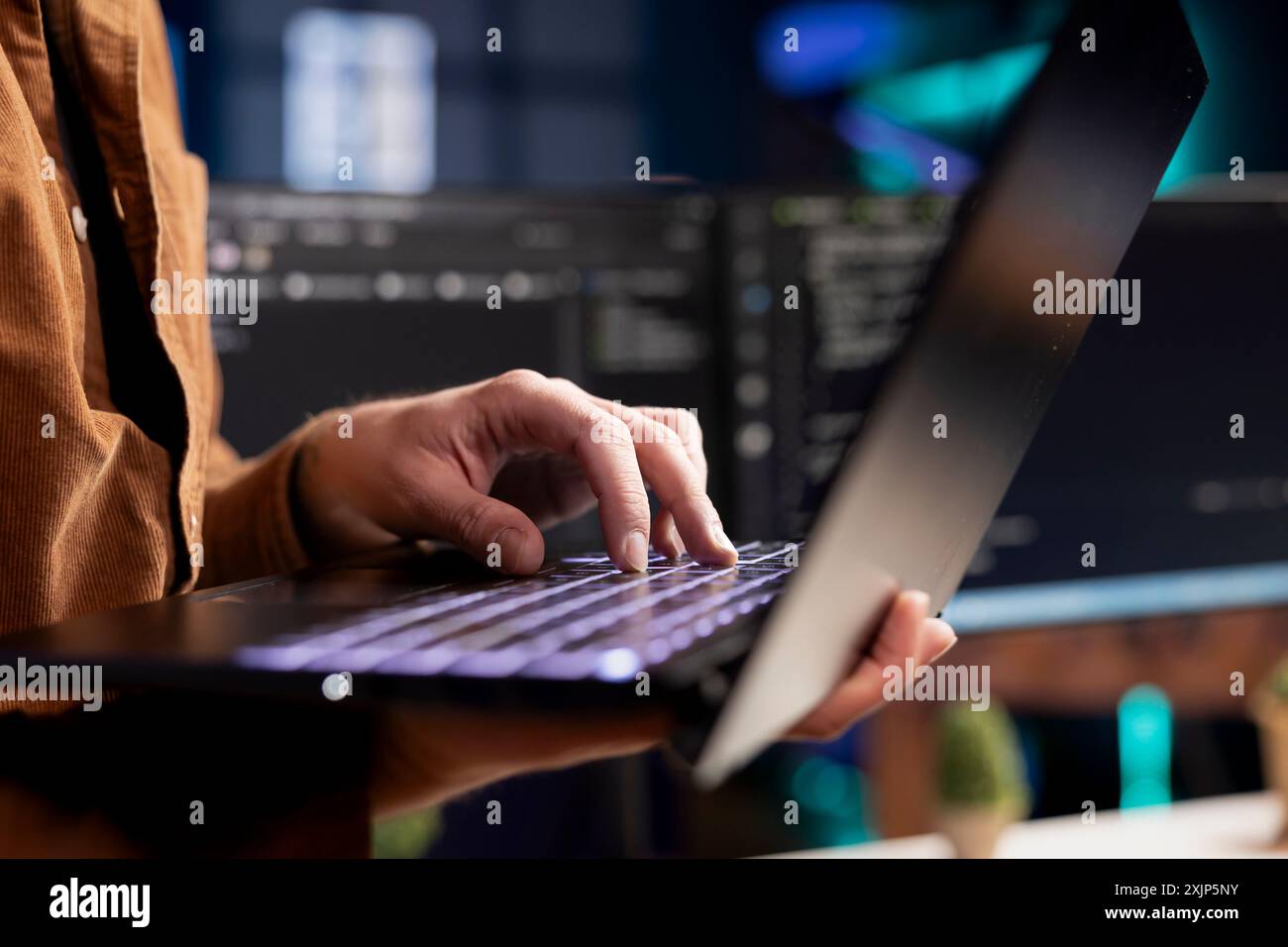 Computer scientist working from home using laptop, testing and deploying programs. Programmer checking code displayed on desktop PC screens in blurry background, close up shot Stock Photo