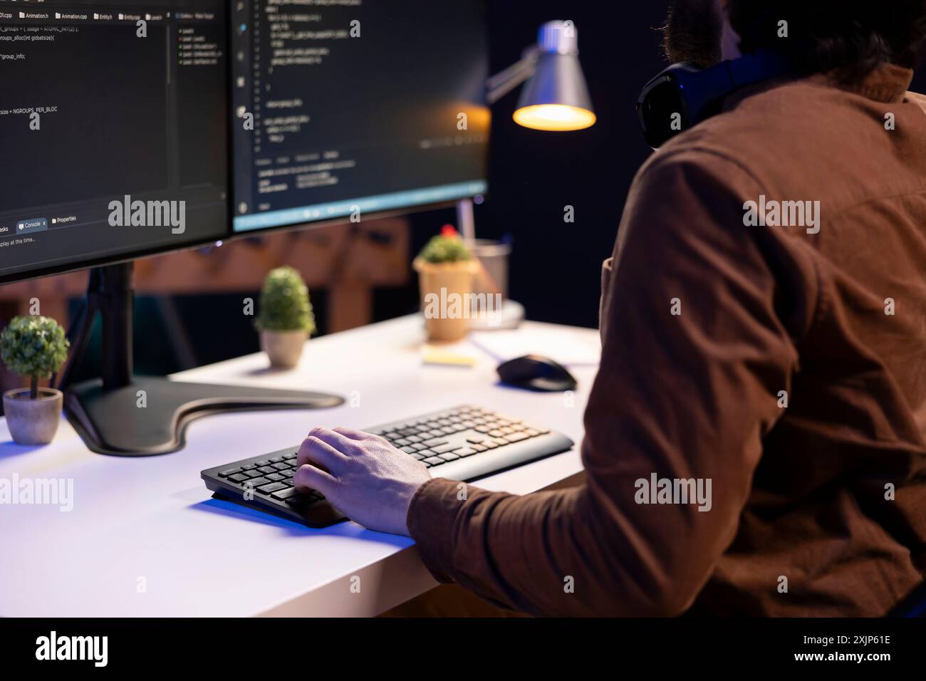 System administrator doing software debugging on PC at home, checking broken lines of code displayed on monitors. IT professional in living room fixing coding problems, typing on keyboard Stock Photo