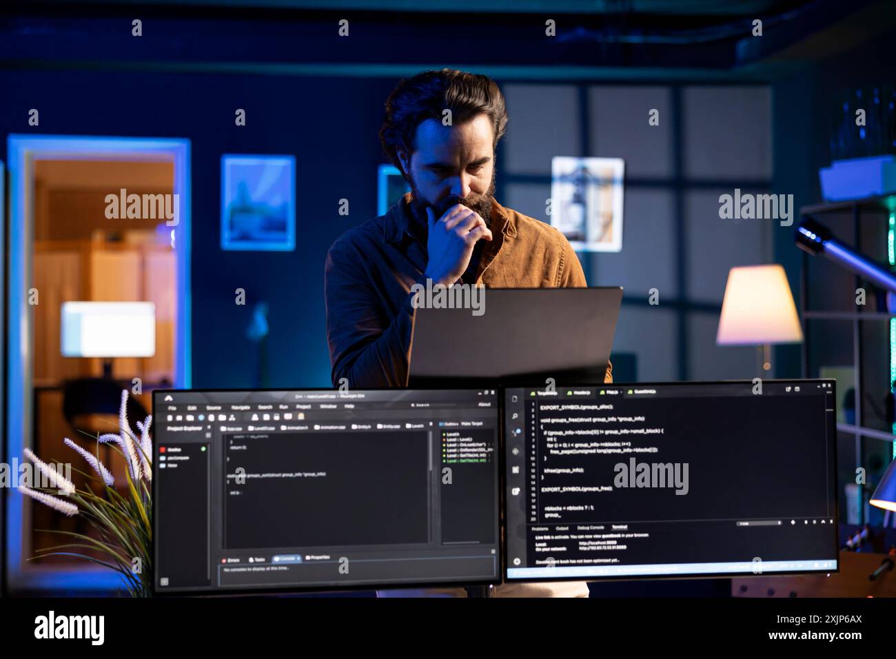 Man working from home developing software in Java programming language using laptop. Programmer walking through apartment thinking how to solve coding problems using notebook Stock Photo