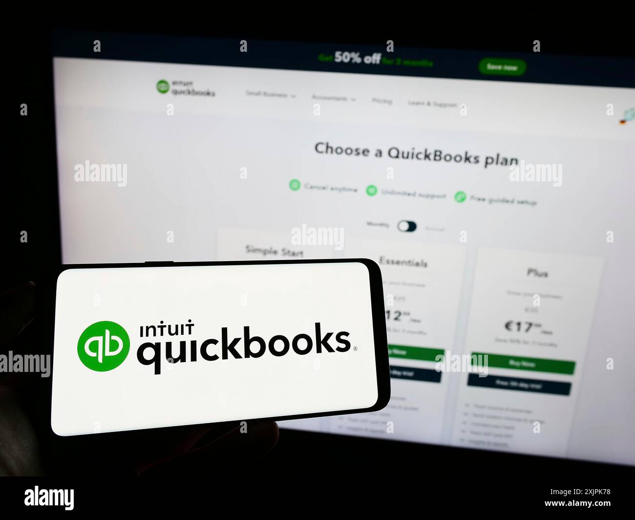 Stuttgart, Germany, 07-09-2023: Person holding cellphone with logo of accounting software QuickBooks on screen in front of business webpage. Focus on Stock Photo