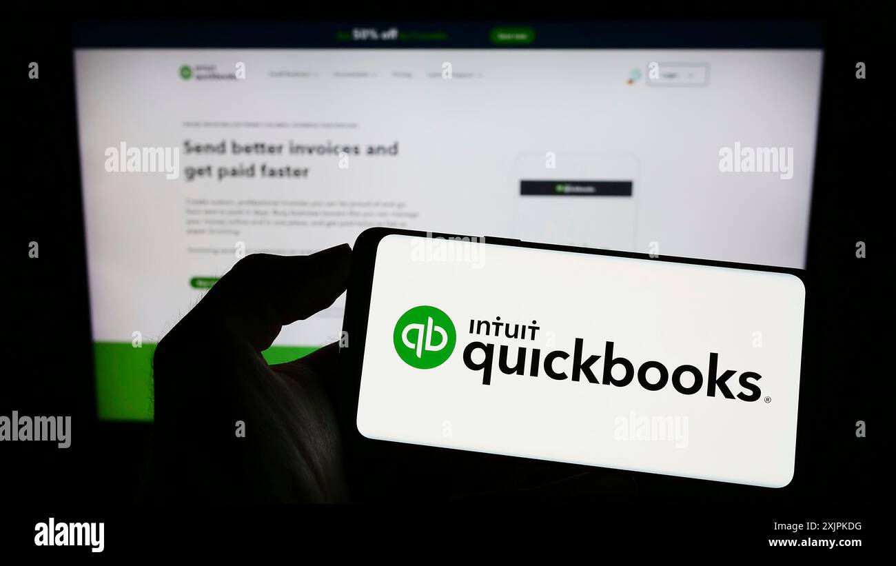 Stuttgart, Germany, 07-09-2023: Person holding mobile phone with logo of accounting software QuickBooks on screen in front of business web page. Stock Photo
