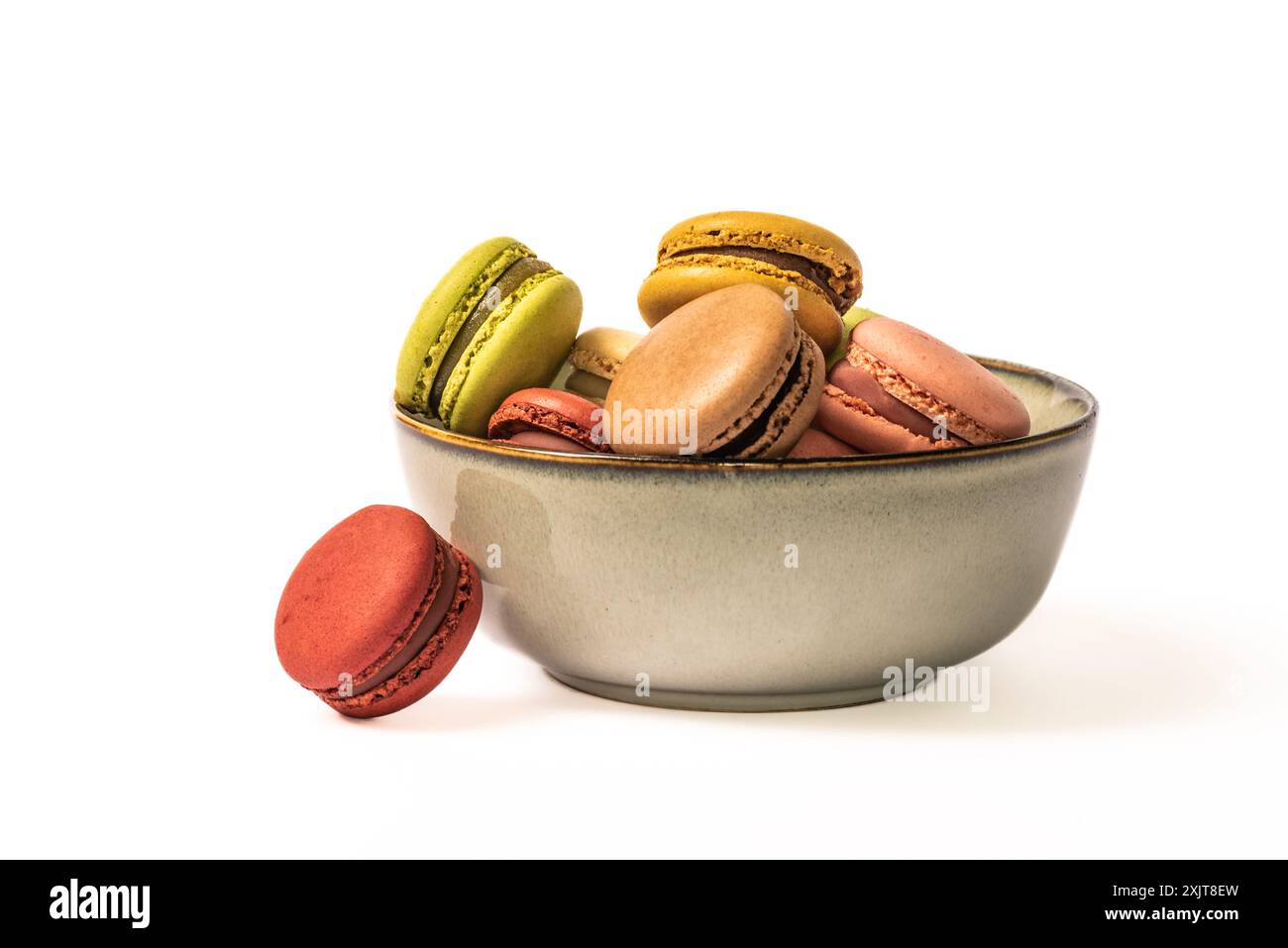 A close-up shot of a ceramic bowl filled with colorful macarons, each with a delicate filling, against a white background. The bowl is a pale brown wi Stock Photo