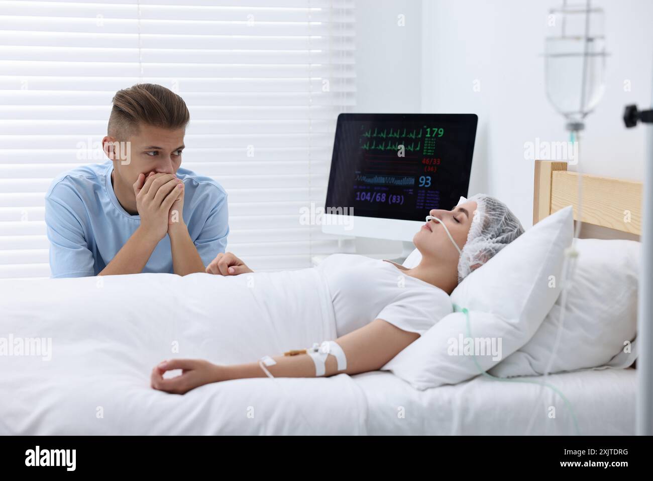 Coma patient. Sad young man near his unconscious wife in hospital Stock Photo