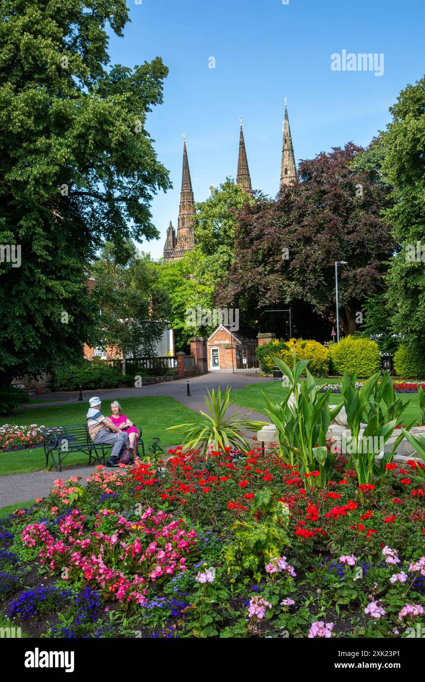 Couple enjoying the summer sunshine in the formal  floral flower gardens of  Beacon park Lichfield Staffordshire England UK with the cathedral behind Stock Photo