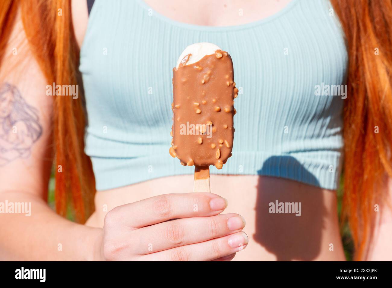 A young woman enjoys a chocolate and almond covered ice cream on a sunny summer day Stock Photo