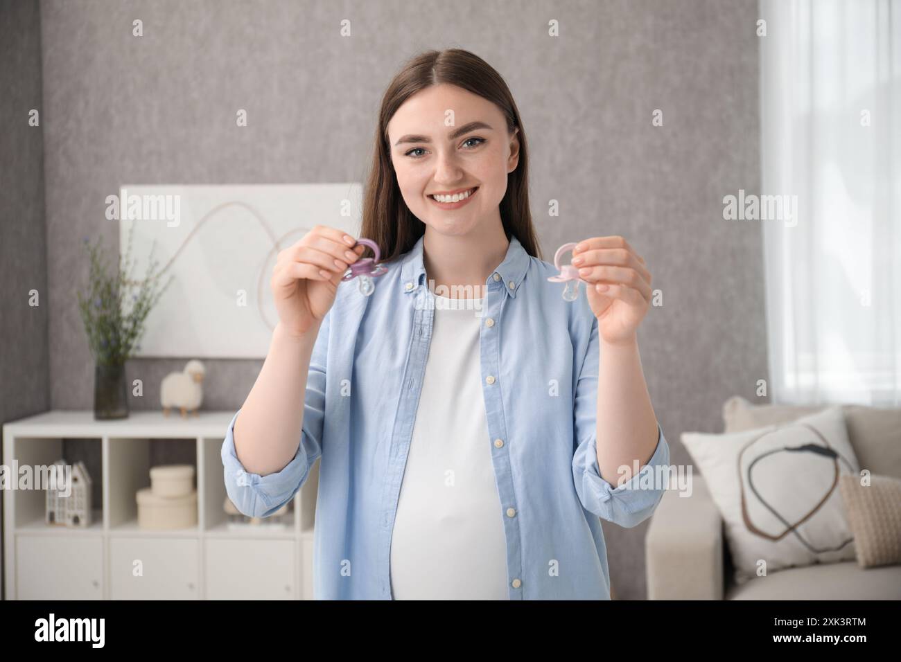 Expecting twins. Pregnant woman holding two pacifiers at home Stock Photo