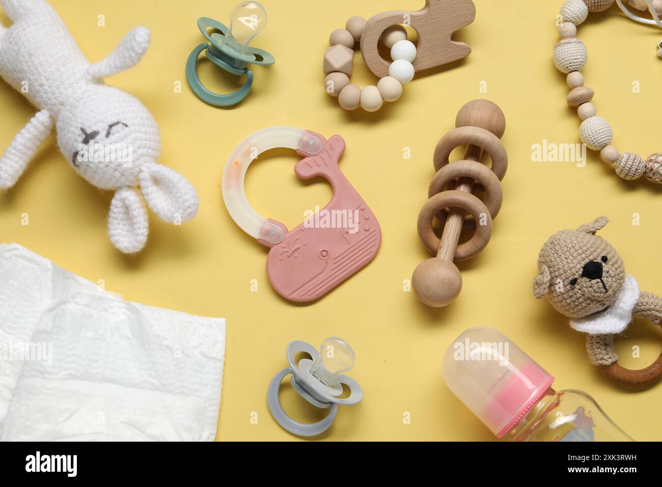 Colorful rattles, diapers, bottle and pacifiers on yellow background ...