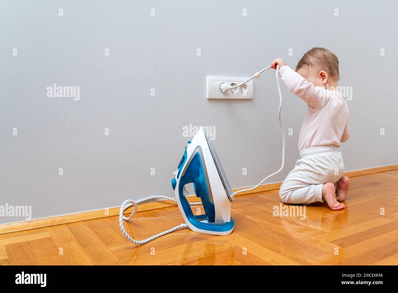 The child pulls the electrical plug out of the socket to let the iron cool down. Stock Photo