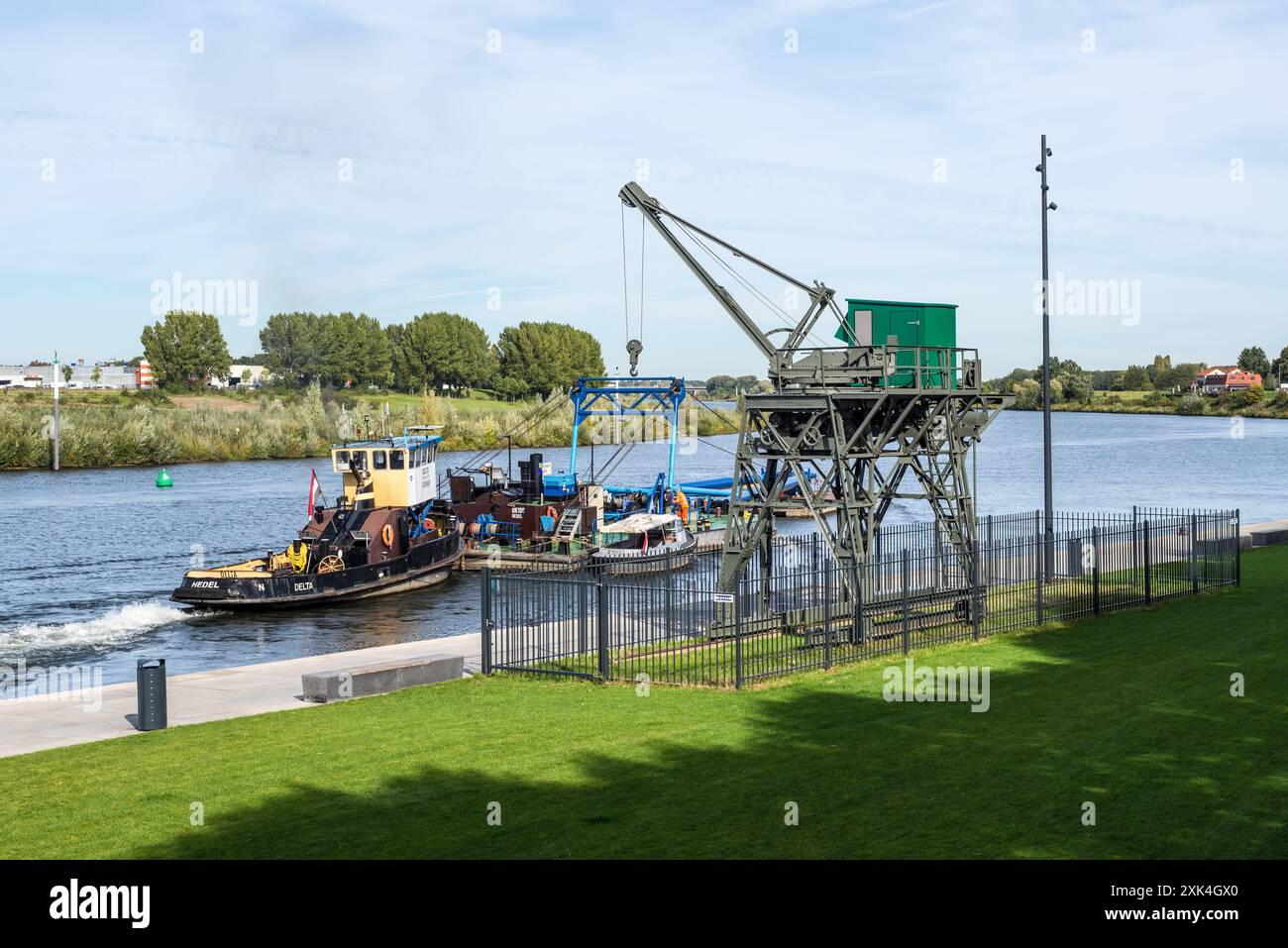 Venlo, The Netherlands - September 25, 2023: Scene on the Meuse river with an old harbor crane as a monument and a tugboat with special barges in Venl Stock Photo