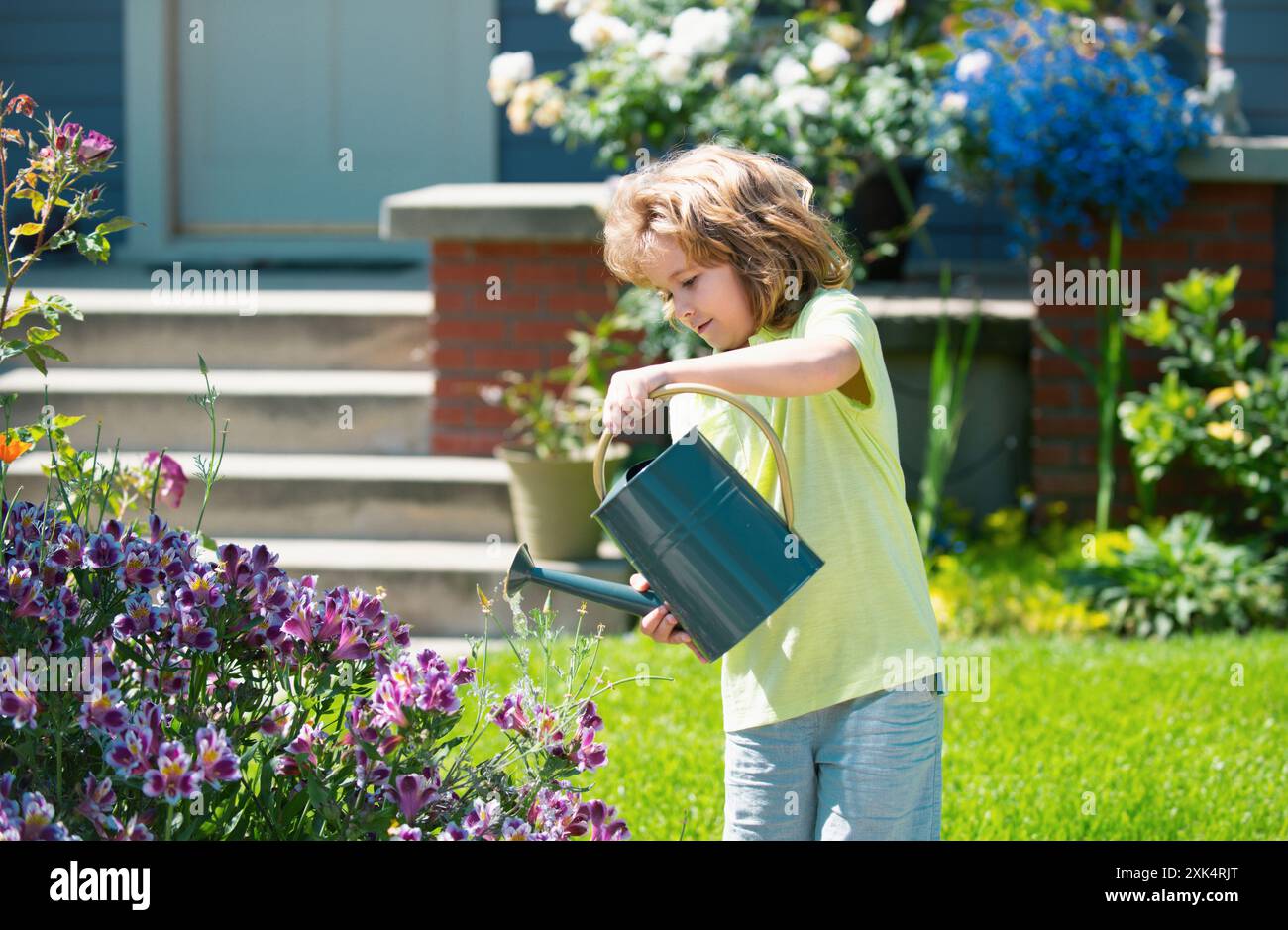 Cute little toddler boy watering plants with watering can in the garden