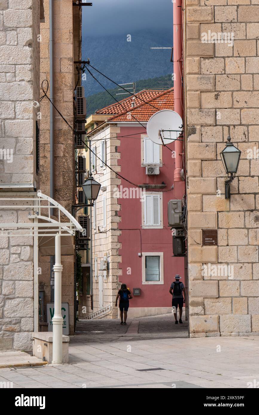 narrow street in Makarska city, Dalmatia, Croatia. Walking tourists. Man and woman. A popular tourist destination for summer holidays in Croatia. Stock Photo