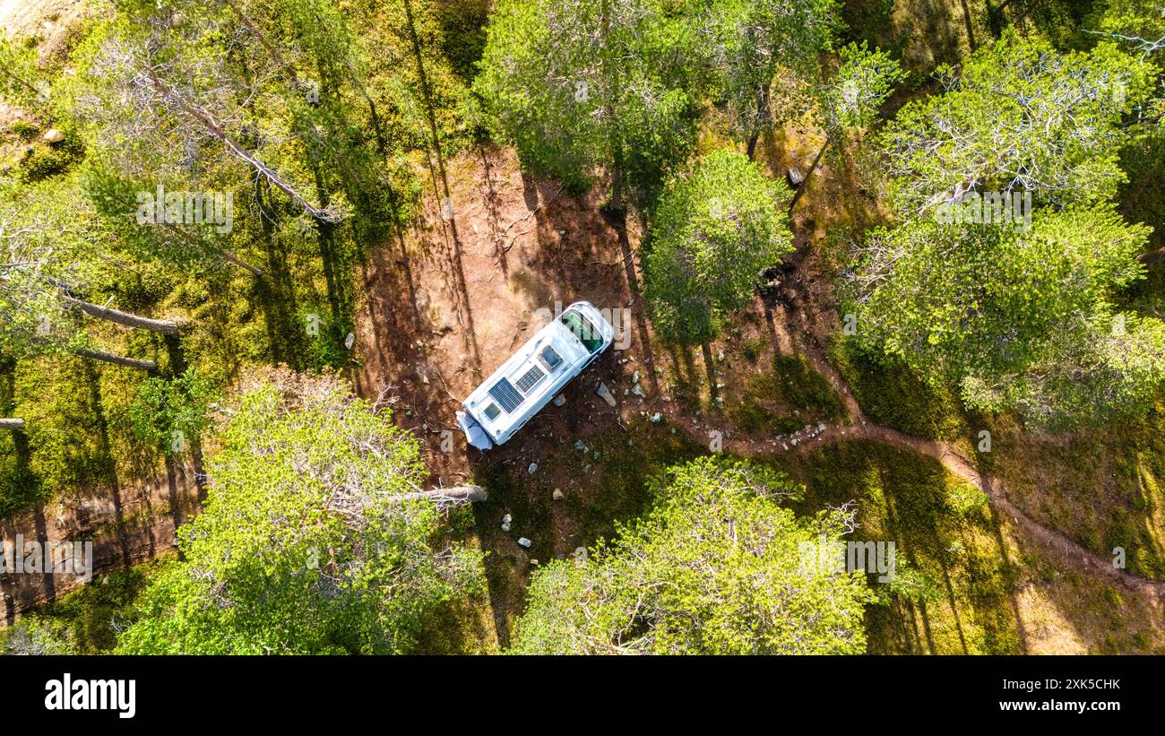 An aerial view of a white camper van parked in a clearing surrounded by ...
