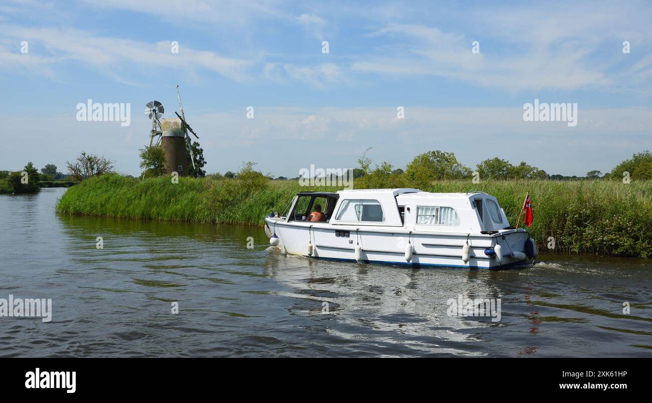Broads Cruiser on the river Ant Norfolk Boards windmill in background. Stock Photo