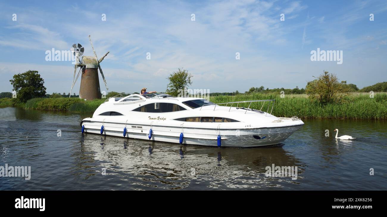 Broads Cruiser on the river Ant Norfolk Boards windmill in background. Stock Photo