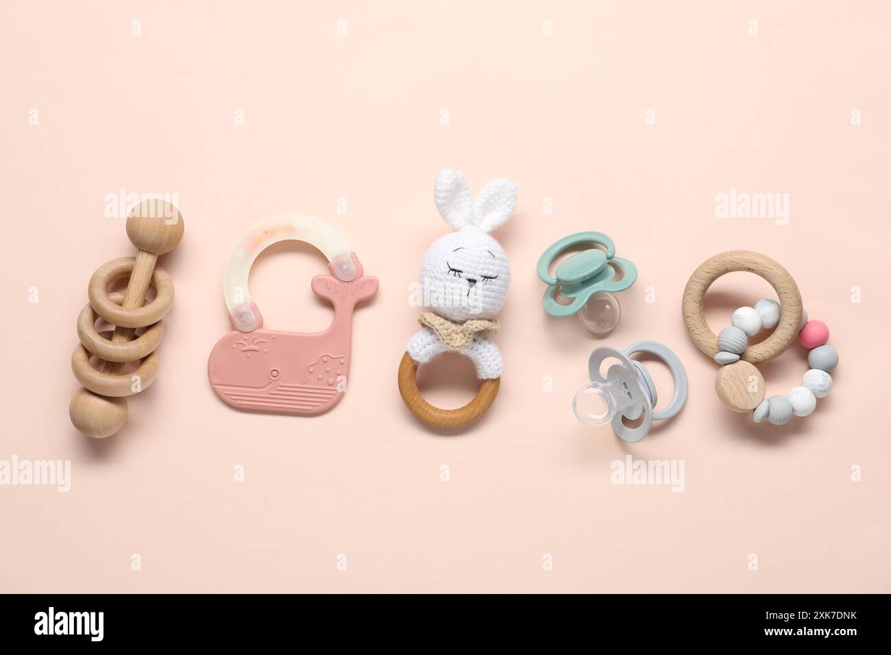 Different rattles and pacifiers on light pink background, flat lay ...