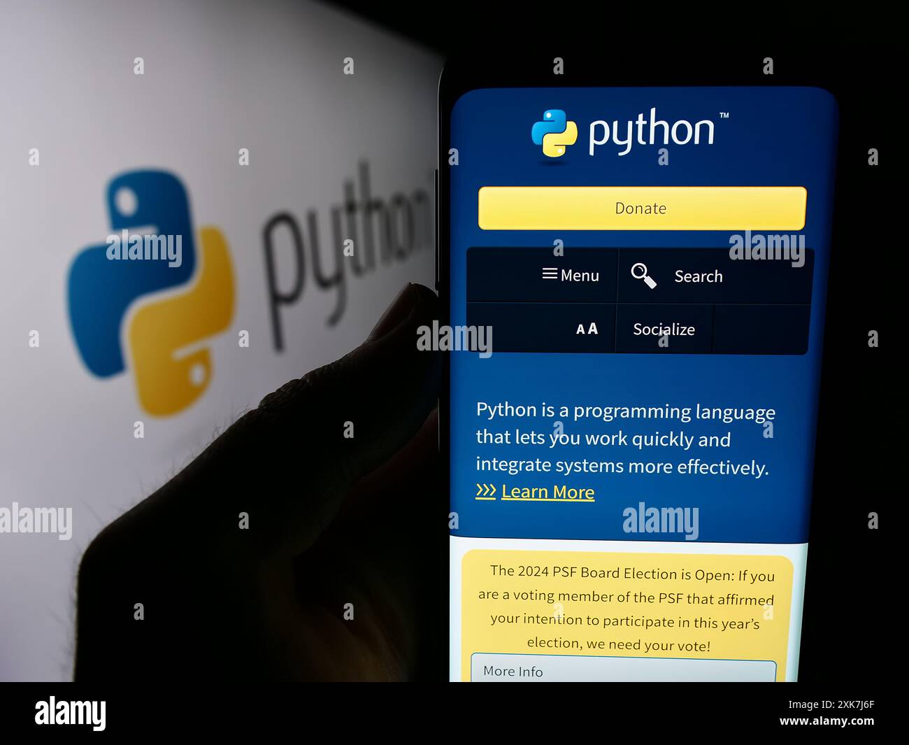 Person holding mobile phone with website of organisation Python Software Foundation (PSF) in front of logo. Focus on center of phone display. Stock Photo
