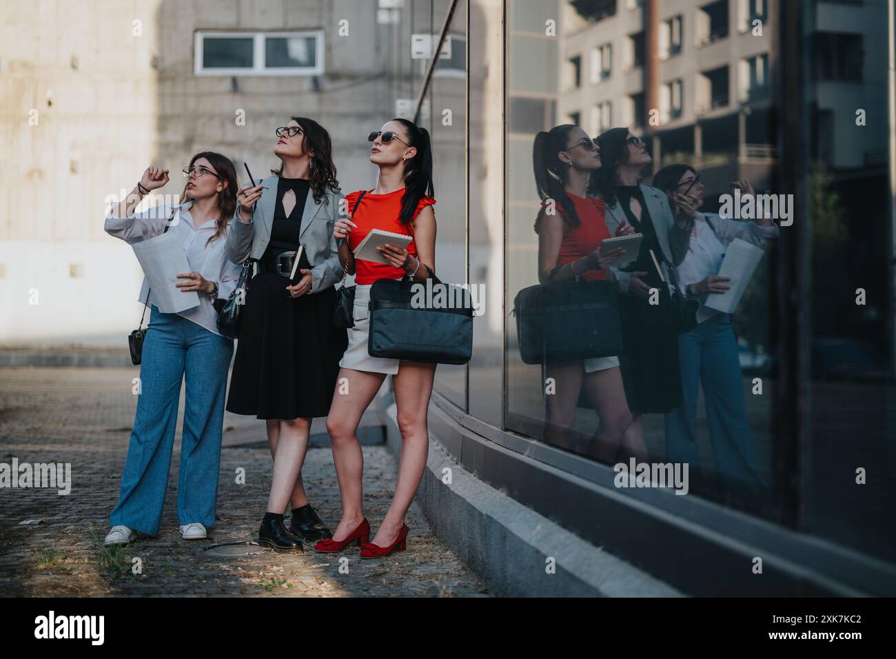Three businesswomen collaborating outdoors, analyzing blueprints and planning project Stock Photo