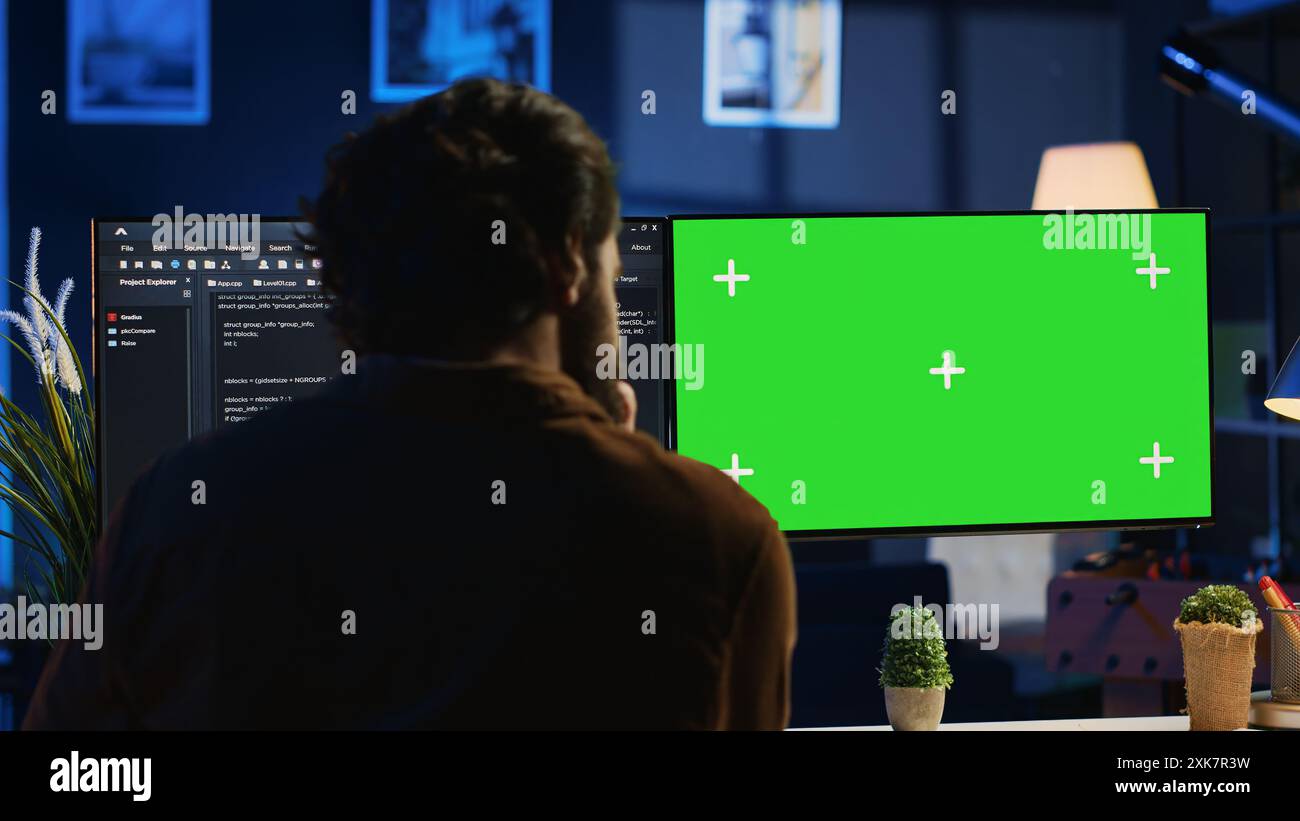 Programmer typing complex code on green screen computer in neon lit home office, developing software application. Teleworking IT specialist doing remote project tasks on mockup PC monitor, camera A Stock Photo