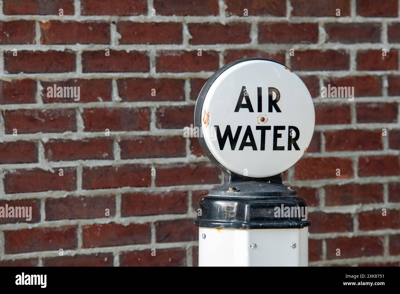 A vintage red brick wall with grey mortar. There's an antique air and water pump for tires at a garage. The sign's lettering is black on white. Stock Photo