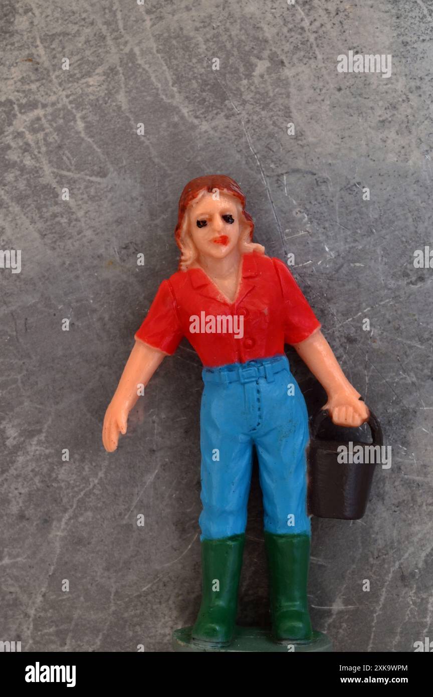 Vintage model of farm girl in red shirt blue jeans and green boots carrying black bucket Stock Photo