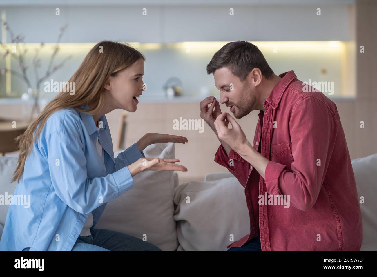 Sign language debate. Romantic couple sits on couch, gesturing actively, arguing using sign language Stock Photo