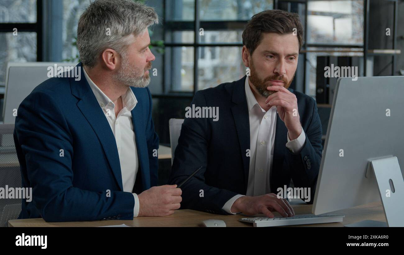 Mature businessman mentoring man discussing project on computer consulting investor client about digital investment in office Caucasian businessmen Stock Photo