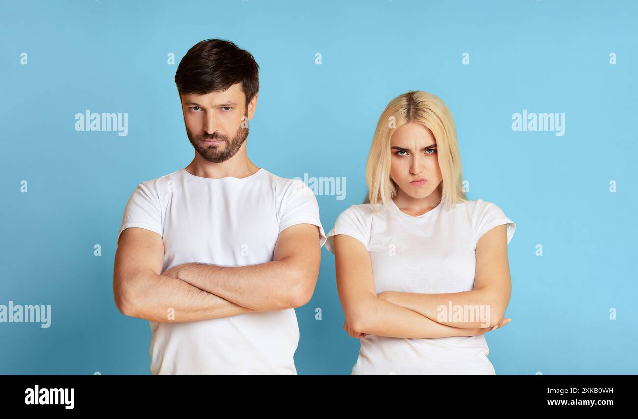 Angry Couple In White Shirts Standing Against Blue Background Stock Photo