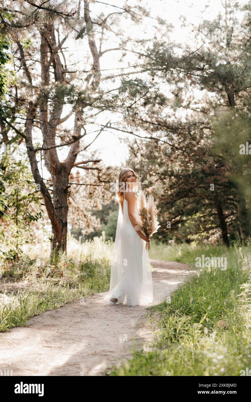 happy bride girl in a white light dress with a bouquet of dried flowers ...