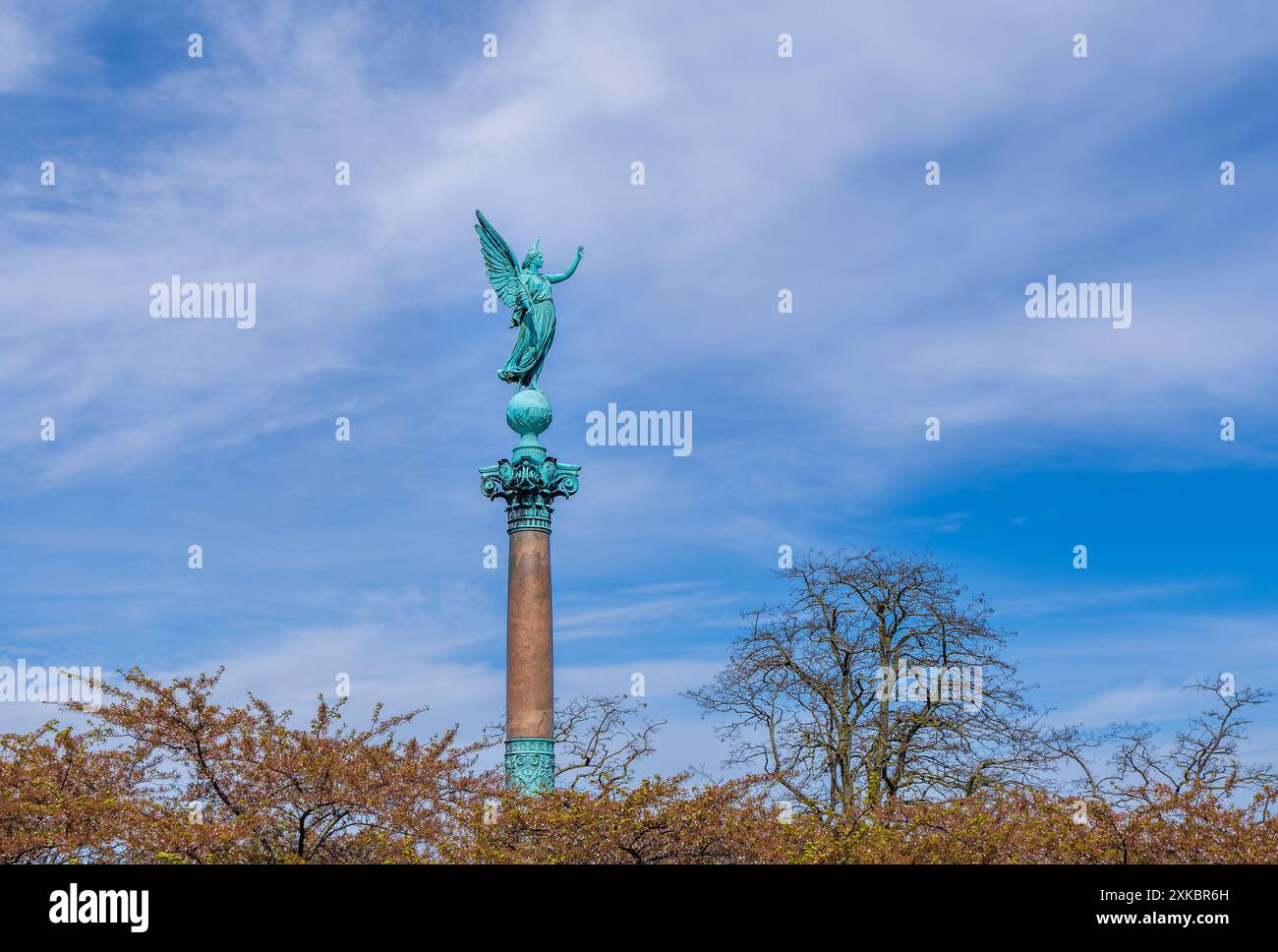 A bronze angel statue sits atop a column among early spring foliage ...