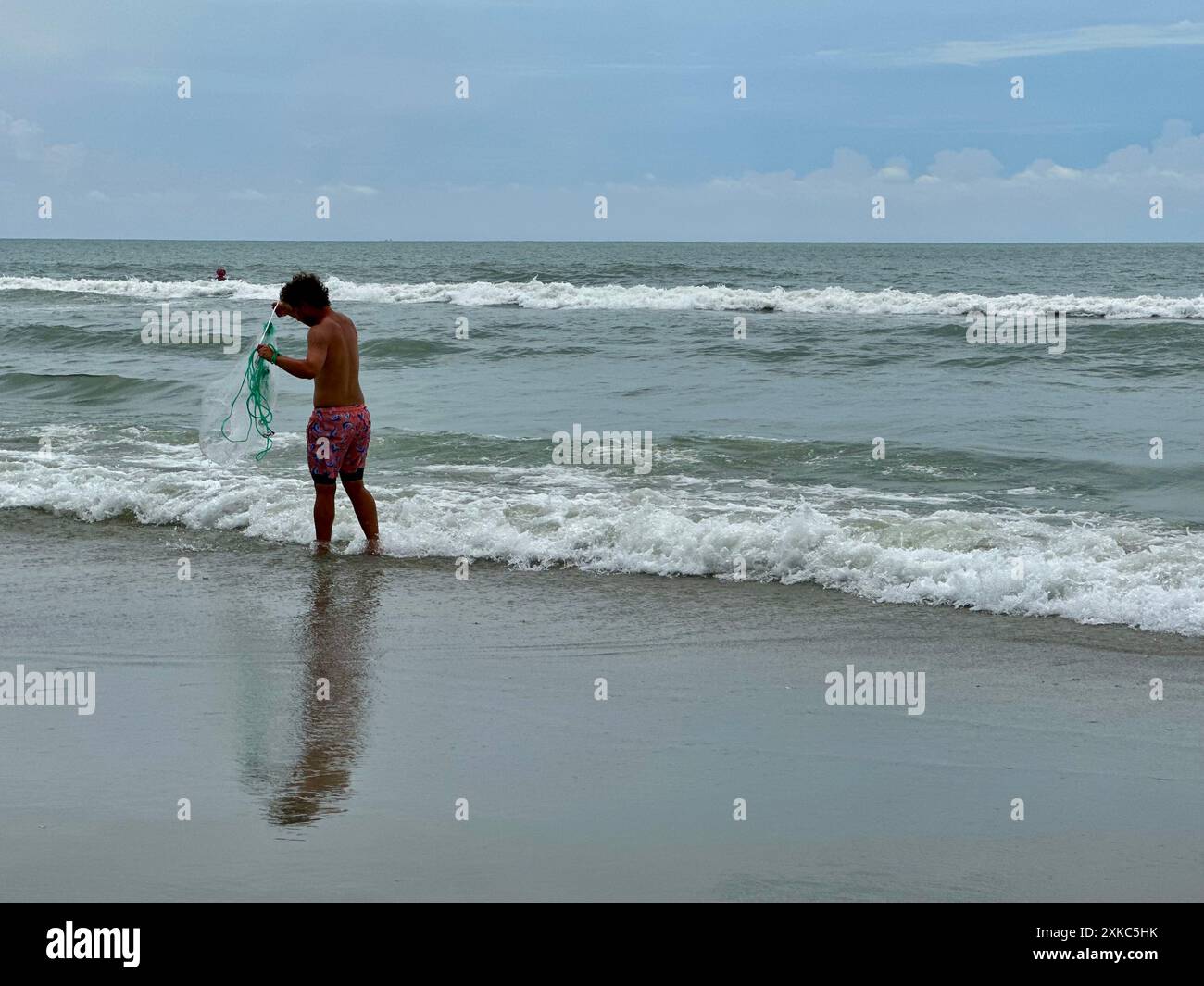 A young man stands at the ocean's edge, casting a net for bait along the hazy shores of North Myrtle Beach, South Carolina. Stock Photo