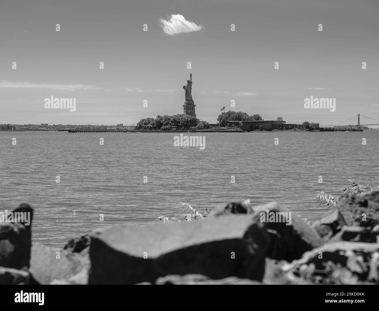 The Statue of Liberty reaches towards the sky, extending her torch to a single cloud in monochrome. Stock Photo