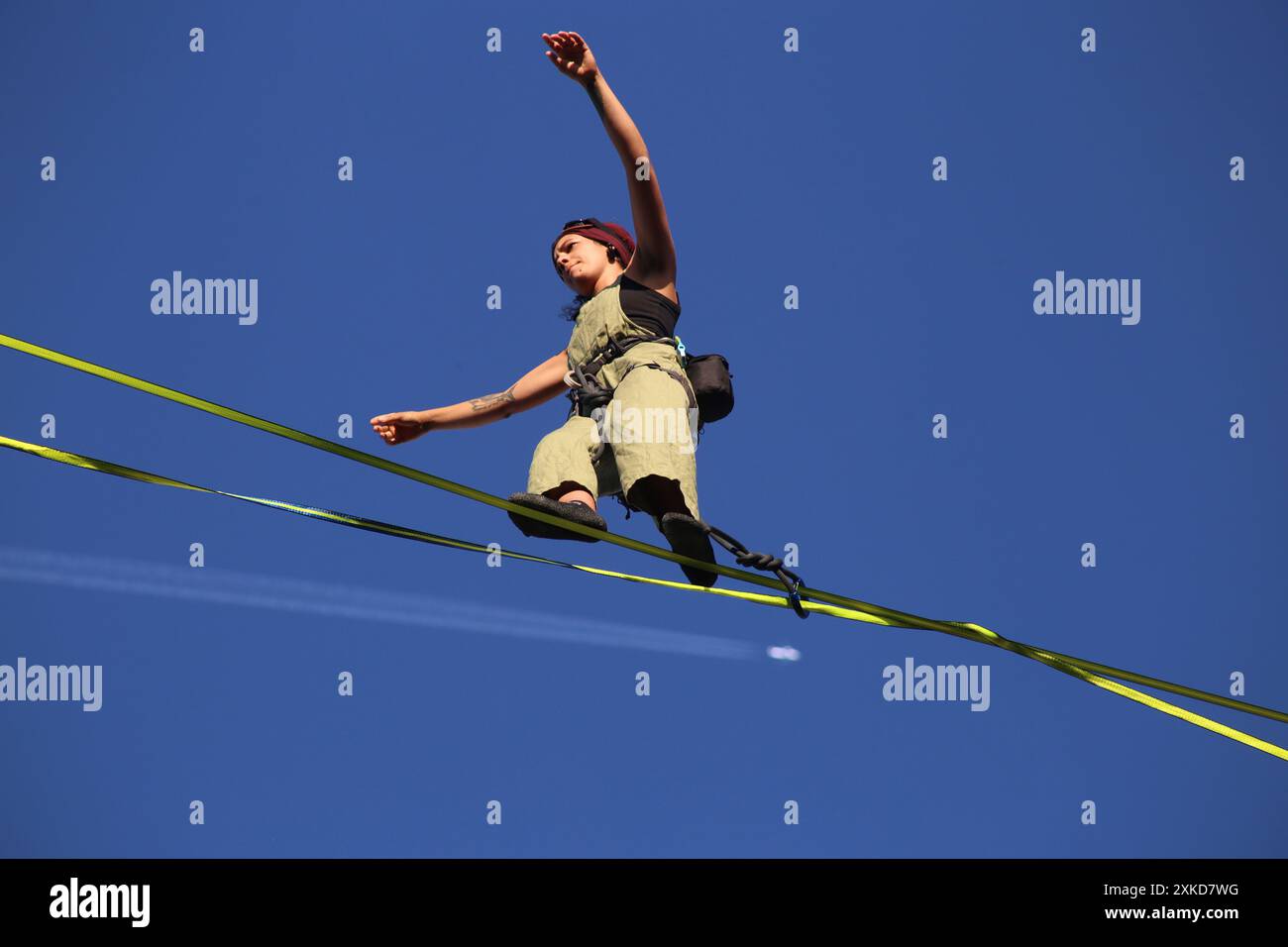 Cracow. Krakow. Poland. Young female aerialist performing tightrope show over the Old Market Place.Plane with contrails seen in the background. Street Stock Photo