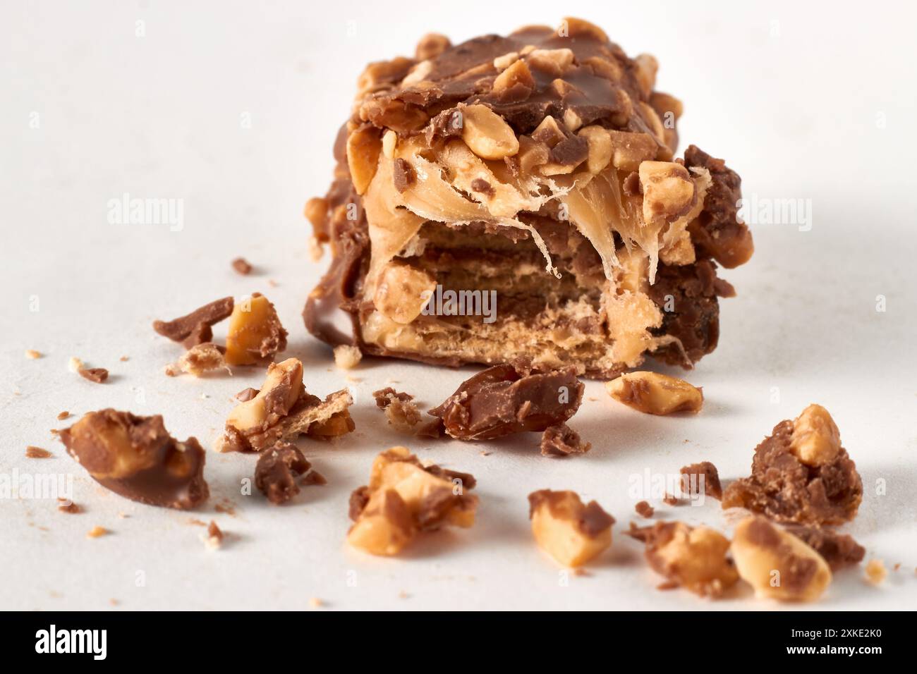 Broken piece of chocolate wafer bar with nuts and caramel in cut and crumbs isolated on white background Stock Photo