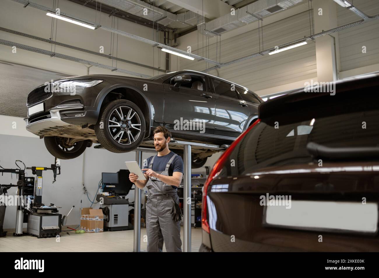 Mechanic using tablet while inspecting elevated SUV in garage Stock Photo