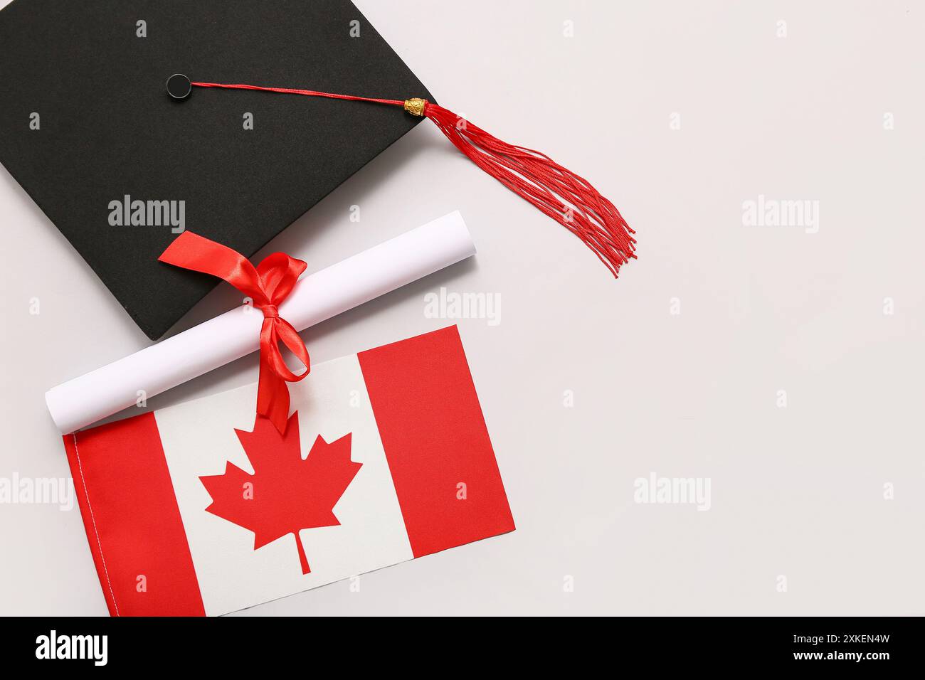Diploma with red ribbon, Canadian flag and graduation hat on white ...