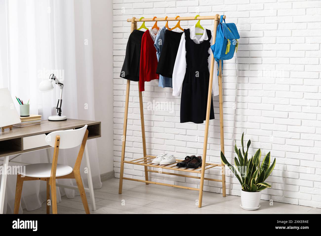Rack with stylish school uniform, houseplant and workplace in light ...