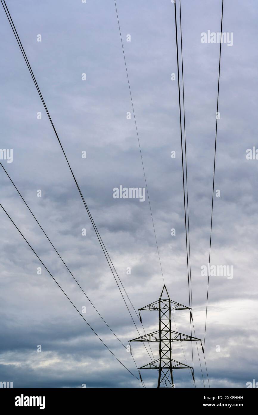 An electricity pylon (132kV overhead line pylon), power lines in front of a cloudy sky and landscape in the background. Wohlen near Bern, Switzerland Stock Photo