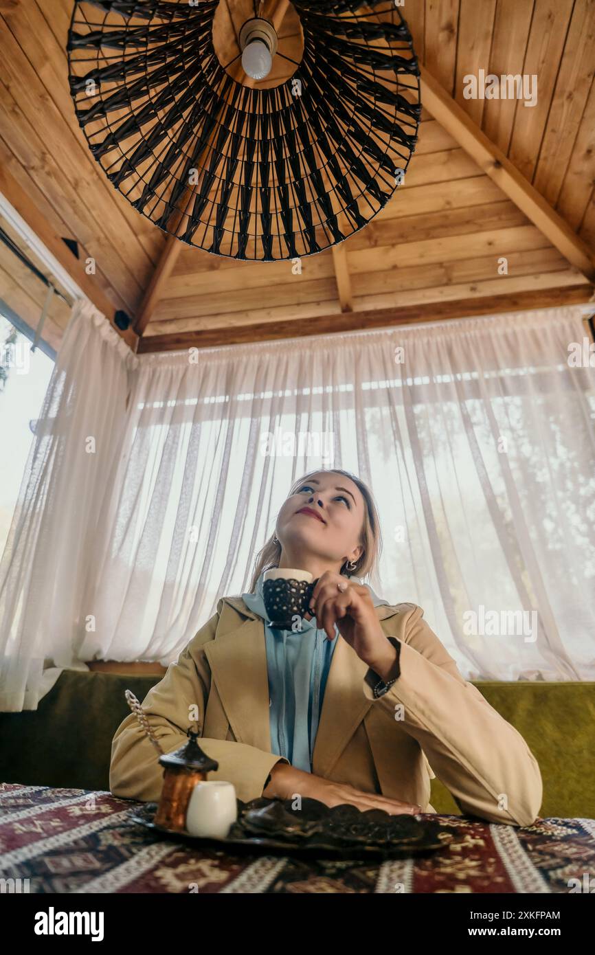 Woman Gazing Upwards While Enjoying a Drink in a Cozy Cafe Stock Photo